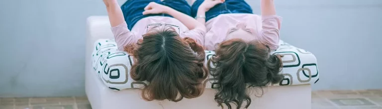 Zwei kleine Mädchen in rosa Shirts liegen nebeneinander auf einem Sessel. Zu sehen sind ihre Haarschöpfe von hinten.